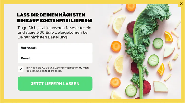 Newsletter sign-up pop-up in German with a yellow border. On the left, the headline “Lass dir deinen nächsten Einkauf kostenfrei liefern!”, a line offering €5 off delivery on the next order for signing up, fields for first name and email, a consent checkbox, and a green “Jetzt liefern lassen” button. On the right, kale, beetroot, cucumber, carrot, orange and lemon slices are scattered on a pale pink background.